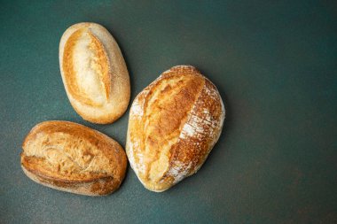 Yeşil bir yüzeyde sergilenmek üzere duran üç çeşit kabuklu ekmek..