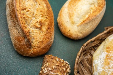 Yeşil bir zemin üzerinde çeşitli taze ekmek somunları sergilenir..