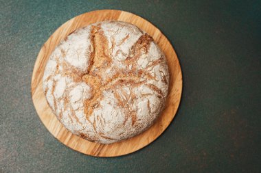 Köy ekmeği ahşap bir kesme tahtasının üzerinde duruyor, kabuğunu gösteriyor..