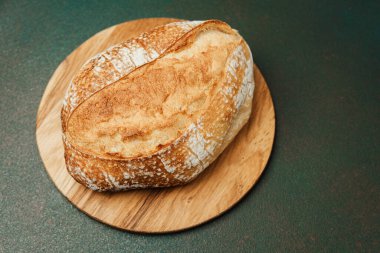 Taze ekşi ekmek, modern bir mutfak ortamındaki ahşap bir tahtanın üzerinde duruyor..