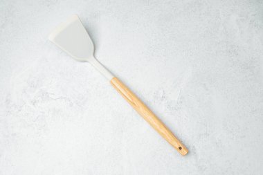 Pürüzsüz bir yüzeyi ve tahta sapı olan bir mutfak spatulası gri arka planda yatar..
