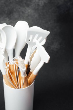 Çeşitli beyaz yemek aletleri, basit bir seramik tutacakta koyu bir arka fona karşı dururlar..