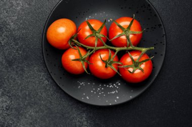 Asmadaki parlak kırmızı domatesler siyah bir tabağa dizilmişler. Mutfak zevki için..