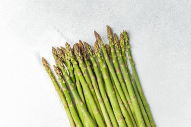 Pürüzsüz gri bir yüzeye serilmiş taze yeşil kuşkonmaz. Pişmeye hazır..