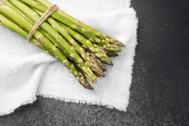 Bir demet canlı yeşil kuşkonmaz basit bir kumaş üzerinde hazırlanmayı bekliyor..