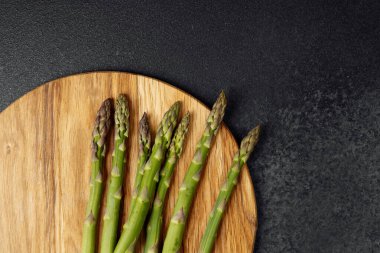 Yeşil kuşkonmaz mızrakları yuvarlak bir tahta kesme tahtasına güzelce yerleştirilmiş..