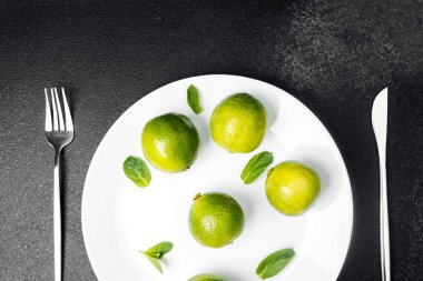 Parlak yeşil limonlar, taze nane yapraklarının yanında beyaz bir tabağa ustalıkla yerleştirilir..