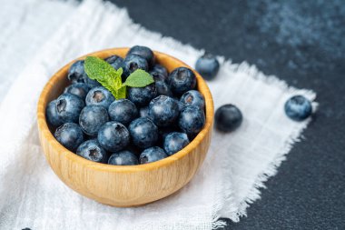 Yumuşak bir kumaş üzerinde nane yapraklarıyla süslenmiş olgun yaban mersinleriyle dolu bir kase..