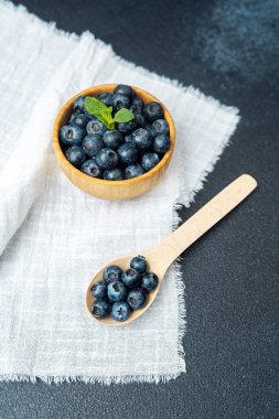 Bir kase taze yaban mersini açık keten kumaşın üzerinde duruyor, yanında da ahşap bir kaşık..