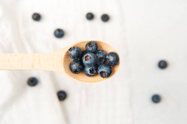 Tahta kaşık olgun yaban mersinlerini yumuşak, hafif bir kumaş zeminine karşı tutar..