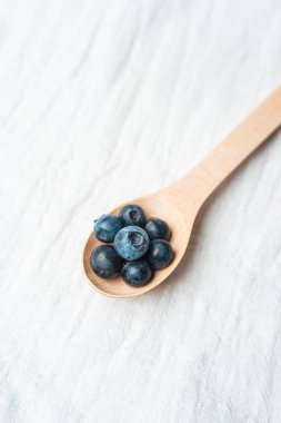 Tahta bir kaşık, hafif ve tarafsız bir zemine karşı birkaç taze yaban mersini taşır..