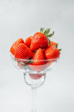 Sulu çilekler cam bir kasenin üzerinde dinleniyor, parlak kırmızı renklerini sergiliyorlar..