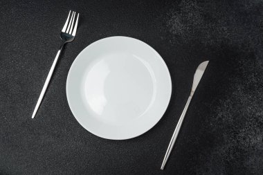 Temiz beyaz bir tabak, arka planda çatal ve bıçakla düzenlenir..