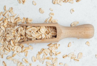 Hafif bir arka planda ahşap bir kepçenin yanında saçılmış yulaflar basit bir sahne oluşturur.