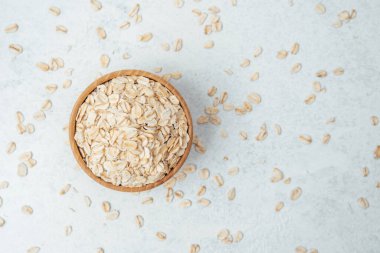 Yulaf dolu ahşap bir kase yakınlarda gevşek taneciklerle hafif bir yüzeyde duruyor..