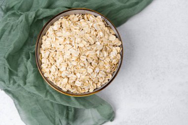 Yuvarlanmış yulaf dolu bir kase yumuşak yeşil kumaşın yanında, açık bir yüzeyde duruyor..