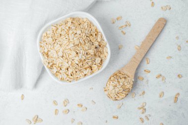 Yuvarlanmış yulaf dolu bir kâse ve yanında pürüzsüz bir yüzey üzerinde duran tahta bir kaşık..