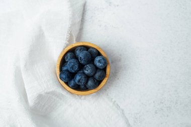 Tahta bir kase olgun, yumuşak beyaz kumaşta taze yaban mersini tutar..