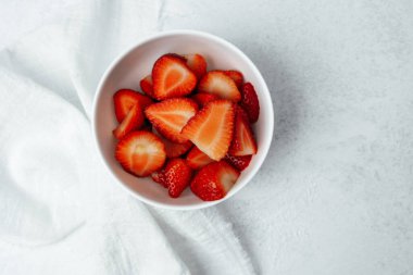 Parlak kırmızı çilekler pürüzsüz bir yüzeyde beyaz bir kasede güzelce düzenlenmiştir..