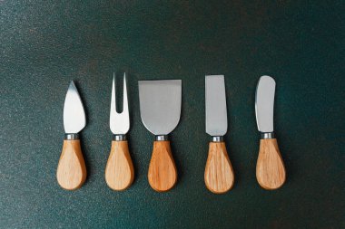 Koyu bir yüzey üzerinde ahşap saplarıyla düzenli çeşitli peynir araçları..