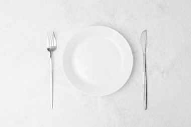 Boş beyaz tabak, çatal ve bıçak içeren minimalist bir masa..