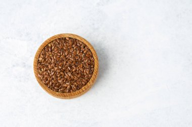 Keten tohumları mermer bir yüzey üzerinde duran yuvarlak bir ahşap kasede sergilenir..