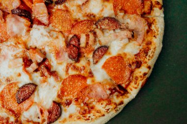 Yeşil arka planda pepperonili, jambonlu ve peynirli lezzetli pizza..