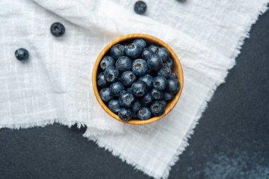 Yaban mersinleri yumuşak beyaz bez bir yüzey üzerinde ahşap bir kasede toplanır..