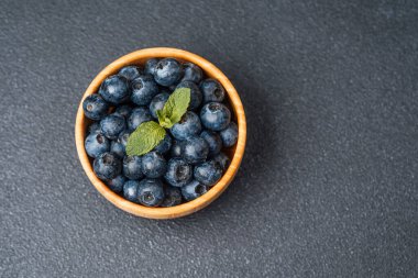 Koyu bir yüzey üzerinde nane yapraklarıyla kaplı taze yaban mersinleriyle dolu bir kase..