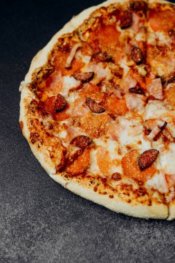 Pepperoni ve sosisli pizza erimiş peynirle birlikte koyu bir yüzeyde duruyor..