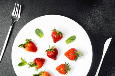 Parlak kırmızı çilekler nane yapraklarının yanına beyaz bir tabağa düzgünce yerleştirilir..