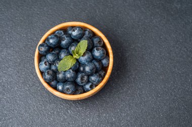 Koyu bir yüzey üzerinde nane yapraklarıyla kaplı taze yaban mersinleriyle dolu bir kase..