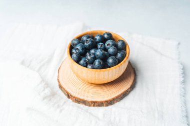 Taze yaban mersiniyle dolu ahşap bir kase bir ağaç diliminde duruyor..