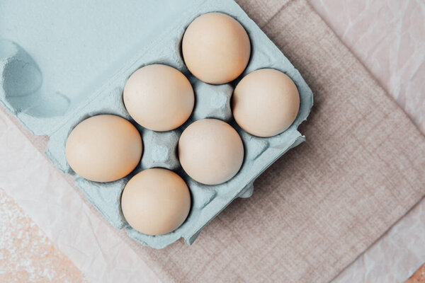 Brown chicken eggs in a blue carton box on light blue background, top view