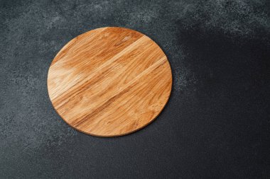 Yuvarlak ahşap bir tahta, yemek servisi için ideal, karanlık bir taş yüzeyde bulunur..