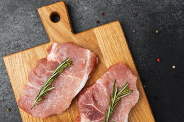 İki çiğ domuz pirzolası taze biberiyeyle kaplı bir tahta kesme tahtasının üzerinde yatıyor..