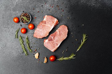 Bitkilerle, kiraz domatesleriyle ve karanlık bir masada baharatlarla çevrili iki parça et..