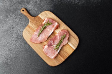 Mutfaktaki ahşap tahtada biberiyeyle süslenmiş iki taze domuz pirzolası..