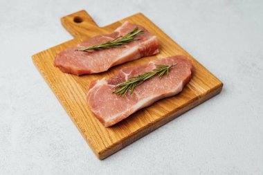 İki çiğ domuz pirzolası ahşap bir kesme tahtasına konur..