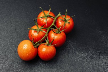 Karanlık bir yüzeyde dinlenen olgun domatesler, taze su damlacıkları sergiliyorlar..