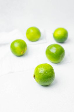 Parlak yeşil limonlar temiz beyaz bir arkaplana dağılmış, tazeliklerini sergiliyorlar..
