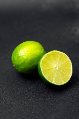 Koyu bir yüzeye yerleştirilmiş parlak yeşil limonlar, açık bir kesikle sulu hamuru ortaya çıkarıyor..
