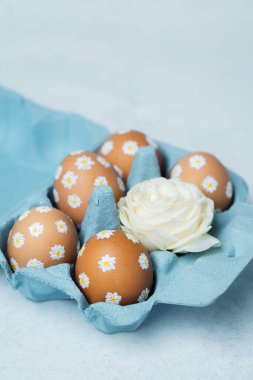 El boyaması Paskalya yumurtaları, papatya desenli beyaz güllü mavi bir karton. Işık arkaplanındaki Paskalya kompozisyonu