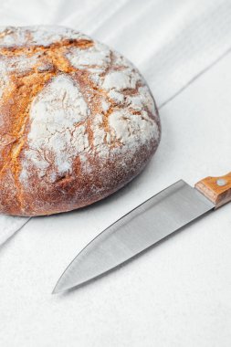 Yuvarlak bir somun ekmek, sade bir mutfak yüzeyinde bıçağın yanında oturur..