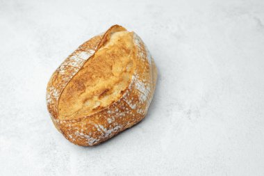 Kabuklu bir zanaatkar ekmek yumuşak gri bir zeminde oturur, altın kabuğunu ön plana çıkarır..