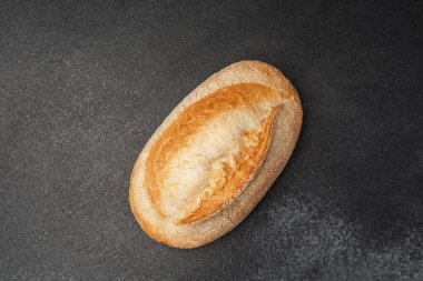 Koyu dokulu bir yüzeye uzanan altın kabuklu ekmek, şeklini sergiliyor..