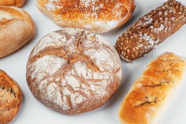 Beyaz bir yüzeye düzgün bir şekilde yerleştirilmiş çeşitli taze ekmek türleri.