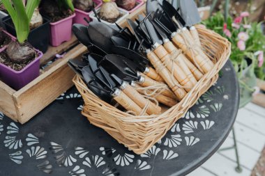 Dışarıdaki dekoratif bir masaya yerleştirilmiş bahçe aletleriyle dolu bir hasır sepet..