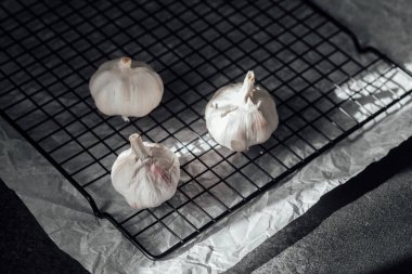 Taze sarımsak ampulleri, yumuşak ışığın altındaki tel soğutma rafında dinleniyor..