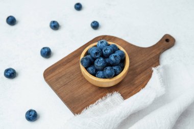 Tahta bir kaseye yerleştirilmiş taze yaban mersini ve yanında kumaş var..